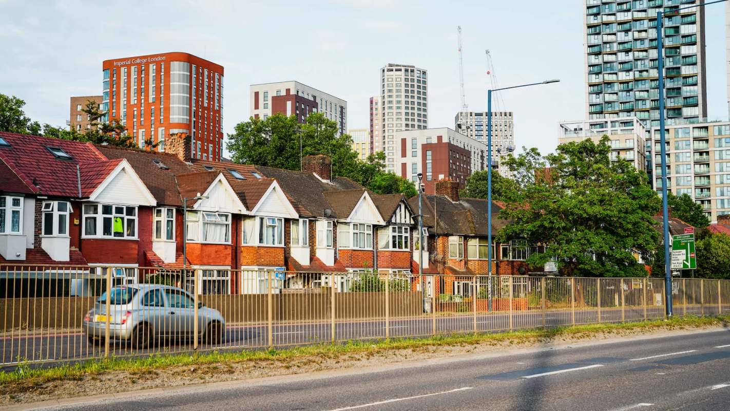 A row of houses in the foreground with modern buildings and trees in the background.