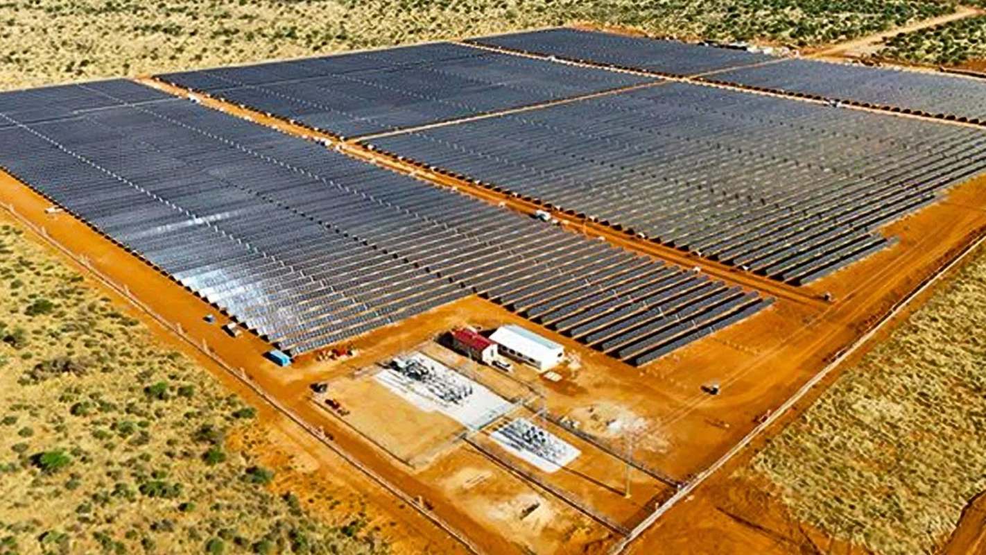 An aerial view of a large solar farm with numerous solar panels on a sandy landscape.