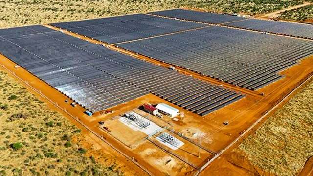 An aerial view of a large solar farm with numerous solar panels on a sandy landscape.