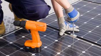 A person installs a solar panel using a drill and a wrench.