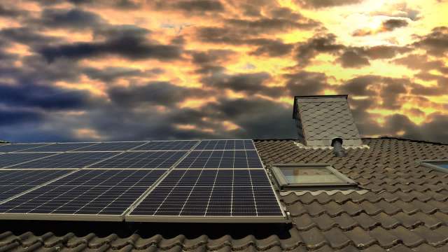 Solar panels on a roof with a chimney against a backdrop of cloudy sunset skies.