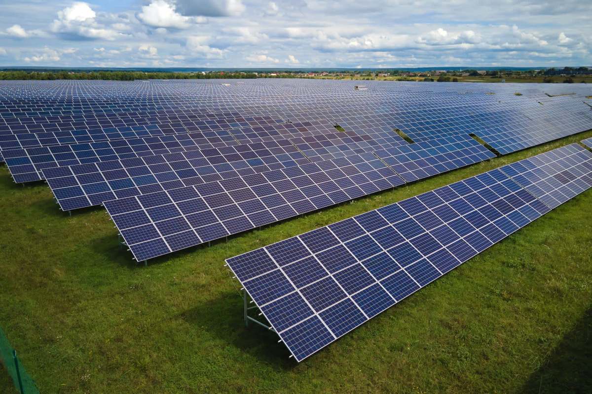 A large solar panel field with rows of solar panels arranged on green grass.