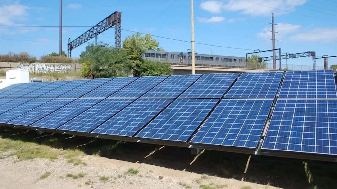 Solar panels installed on ground-level supports with a train in the background.