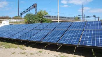 Solar panels installed on ground-level supports with a train in the background.