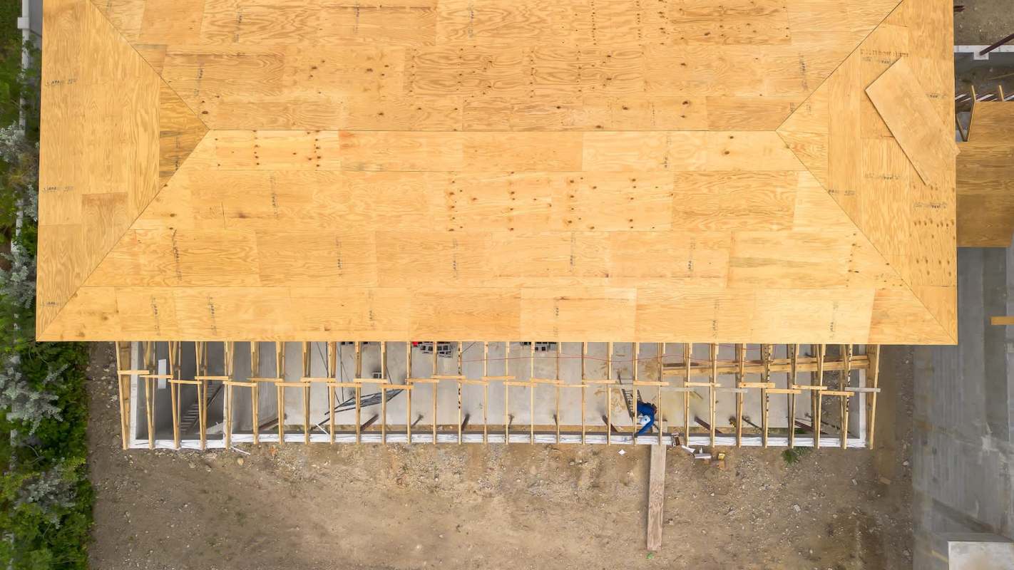 A wooden roof under construction with open framing and a gravel area below.