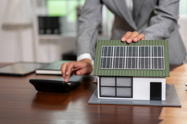 A person works a calculator next to a model home with solar panels