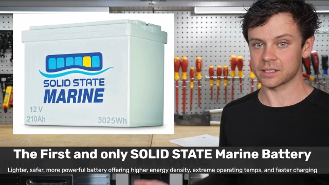 A man stands next to a solid state marine battery displayed on a workshop counter with tools in the background.