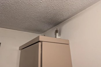 A beige cabinet next to a wall with a visible pipe fitting at the ceiling corner.