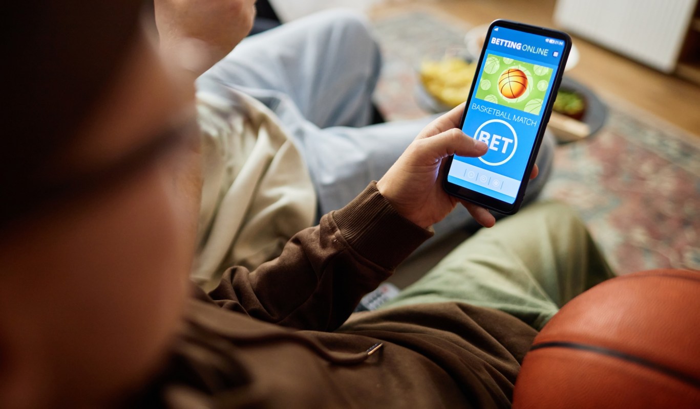 A person using a smartphone to place a bet on a basketball match, with a basketball nearby.