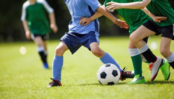 Children play soccer on a grassy field, with a black and white soccer ball at their feet.