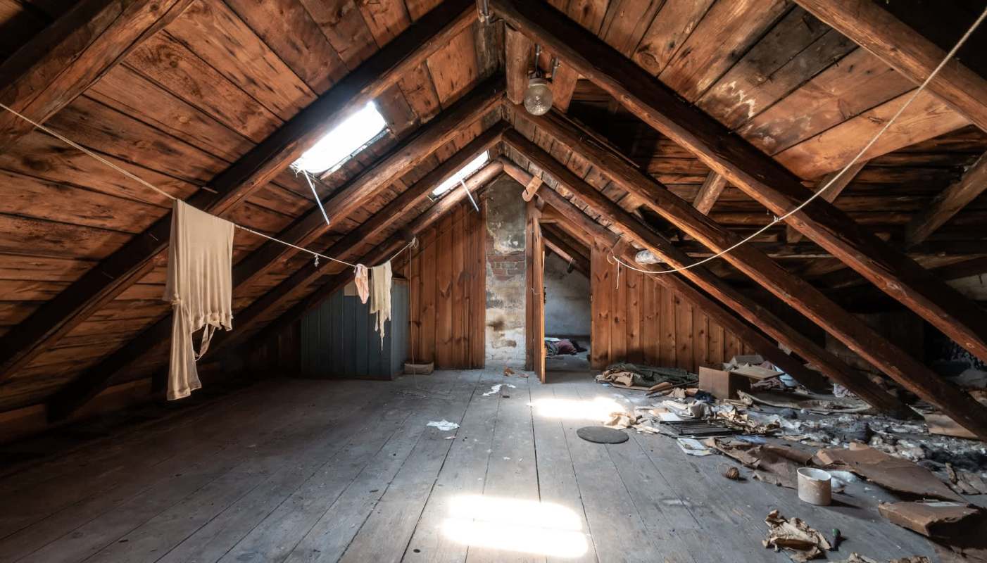 An empty attic with wooden beams, scattered debris, and clothes hanging on a line.