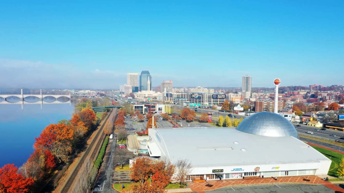 A view of Springfield, Massachusetts, skyline along a river, featuring autumn foliage and a large dome building.