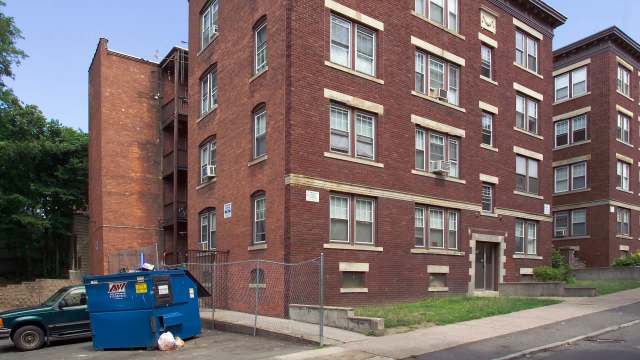 A brick apartment building with multiple windows and a blue dumpster in front.
