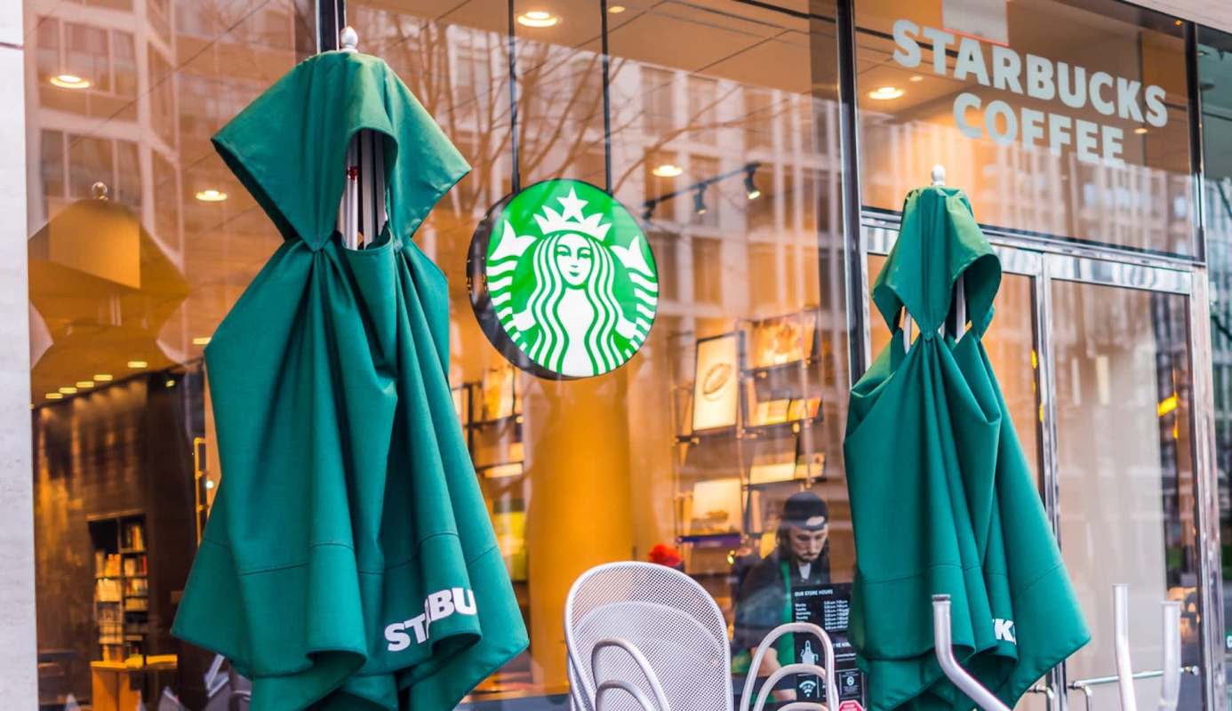 Green umbrellas are closed outside a Starbucks coffee shop, with the company logo visible on the glass door.