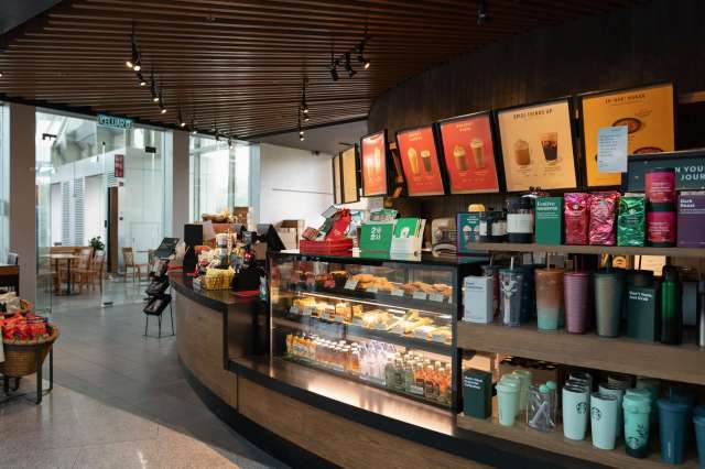 A coffee shop interior featuring a display counter with beverages and pastries, and promotional signs on the wall.