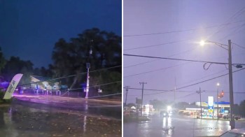 A street scene during a storm with heavy rain, downed power lines, and a gas station in the background.