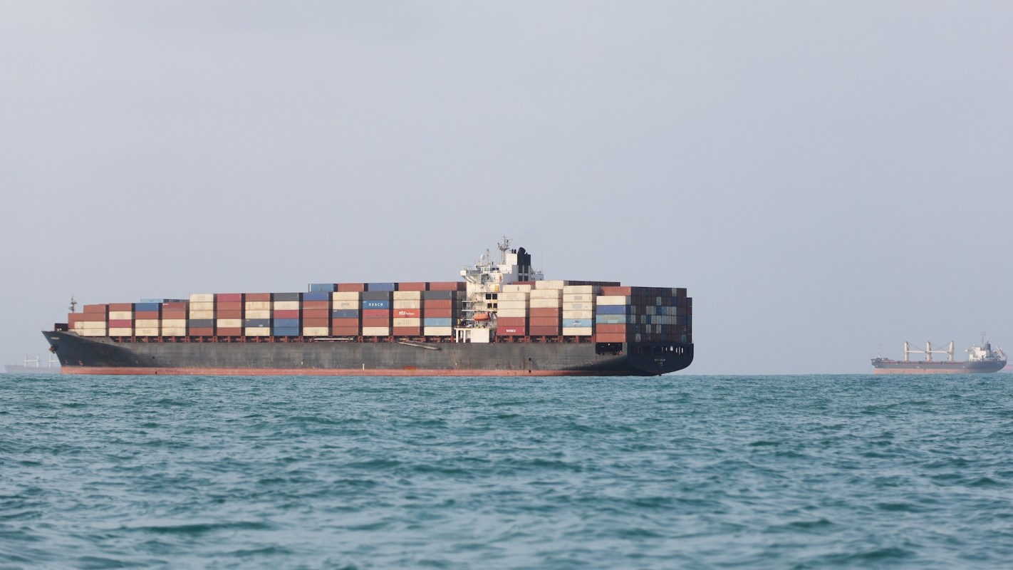 Two cargo ships are anchored in a body of water, surrounded by a calm sea and hazy sky.
