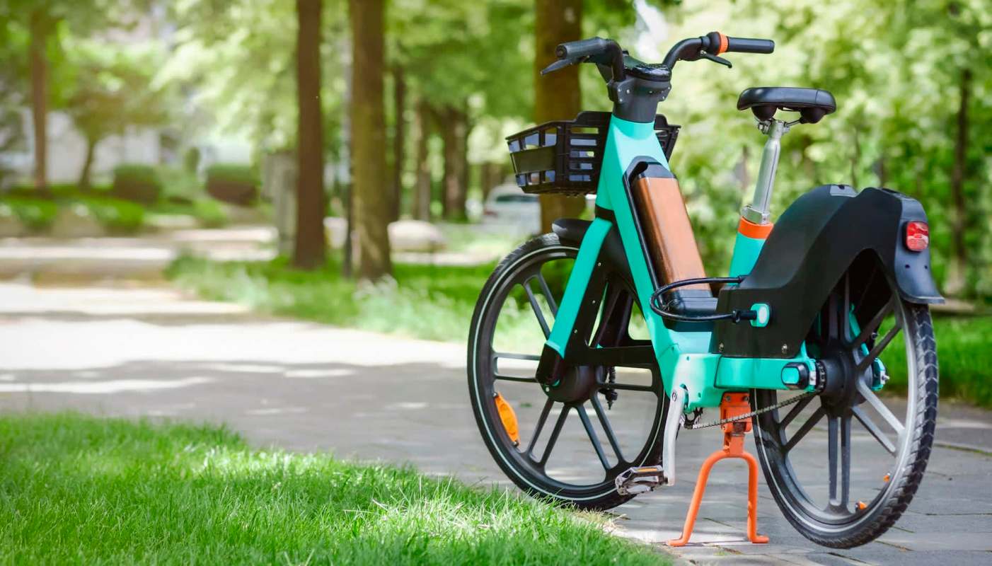 An electric bike parked on a path surrounded by green trees and grass.