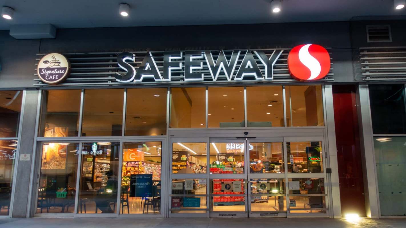 A Safeway grocery store entrance with illuminated signage and large glass doors.