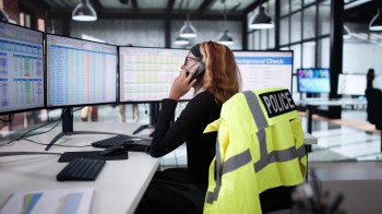 A person speaks on the phone while working at a desk with multiple computer monitors displaying data.