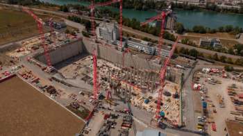 A construction site with cranes, a deep foundation, and various building materials.