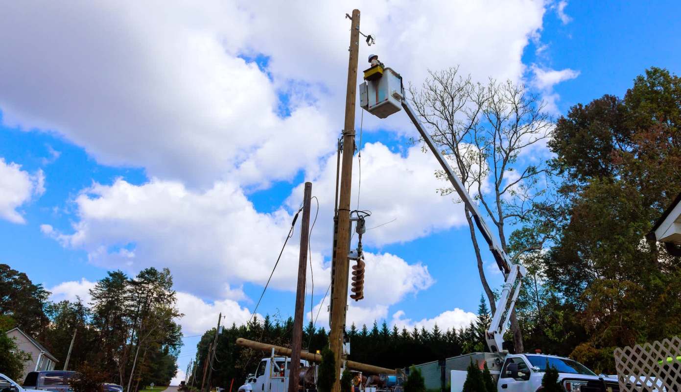 A worker in a bucket truck repairs equipment on a utility pole on a clear day.