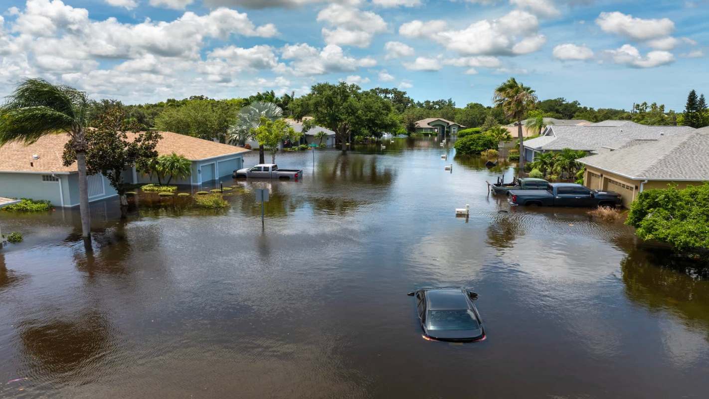 A residential area flooded with water, partially submerging cars and vegetation.