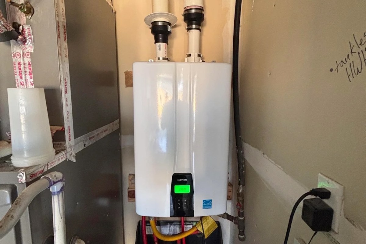 A tankless water heater installed in a utility area next to pipes and electrical outlets.
