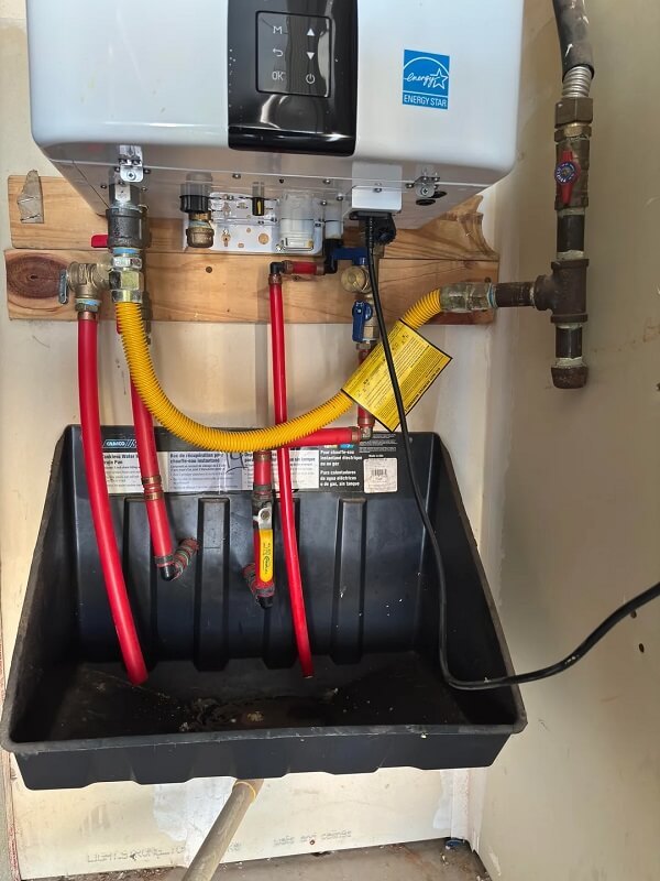 A tankless water heater installed in a utility area next to pipes and electrical outlets.