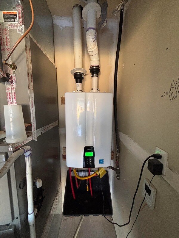 A tankless water heater installed in a utility area next to pipes and electrical outlets.