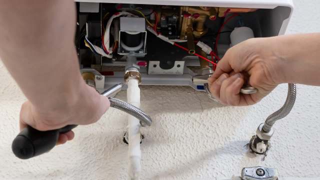 A person is tightening a connection on a plumbing fixture with tools in hand.
