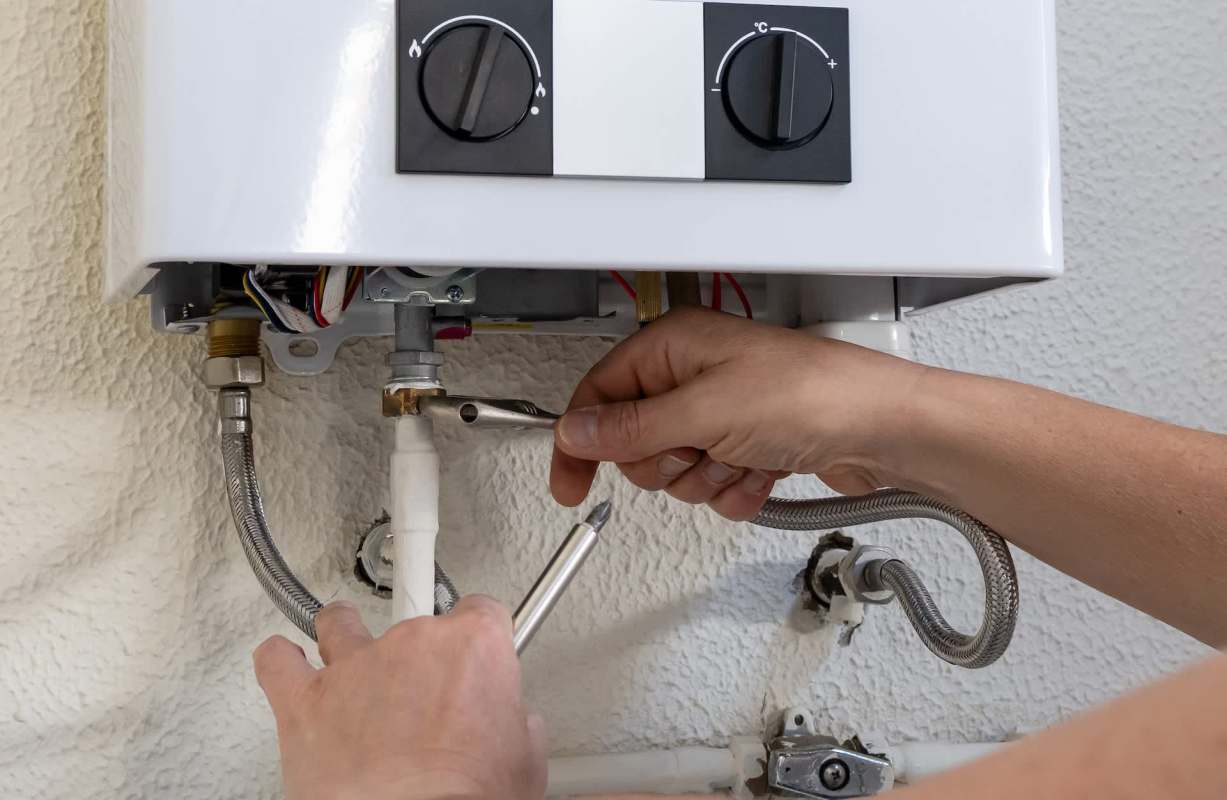 A person adjusting a bolt on a water heater pipe.