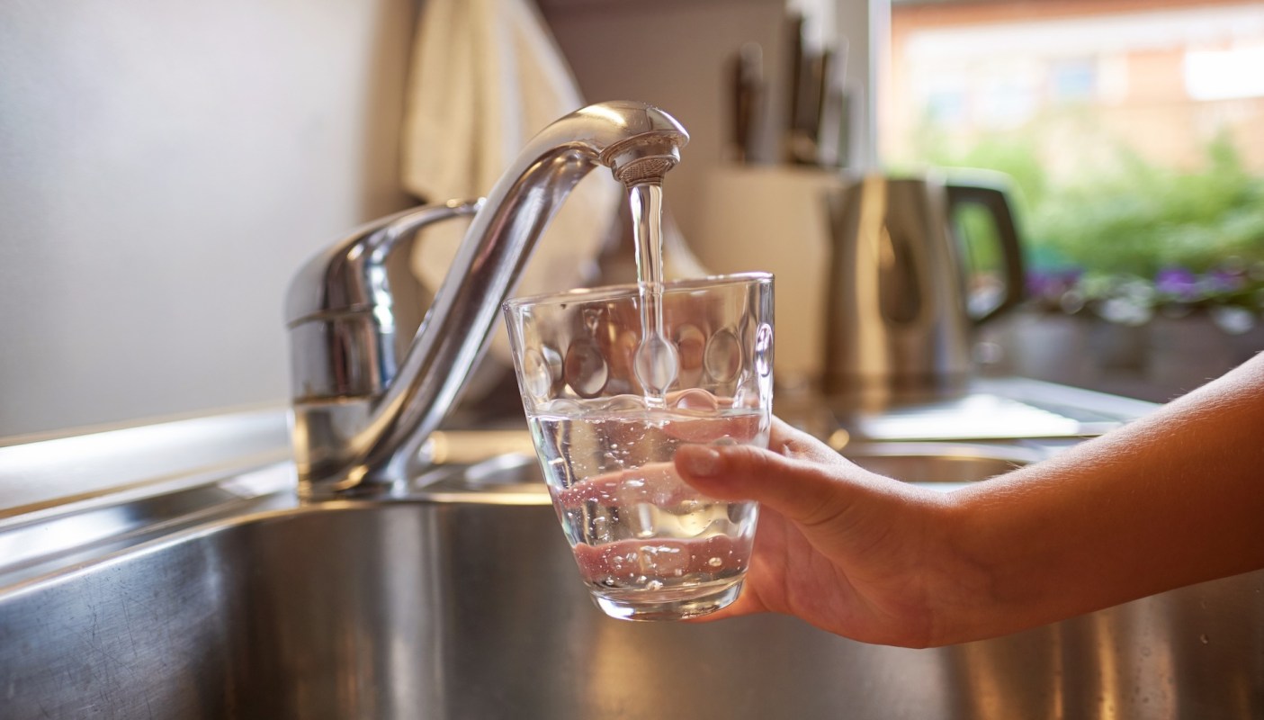 A hand holds a glass filling with water from a kitchen faucet.