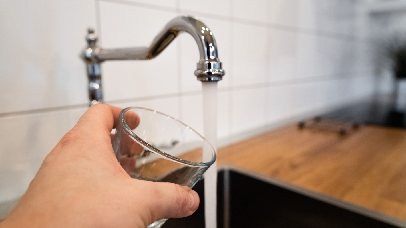 A hand moving to fill a glass under a faucet.