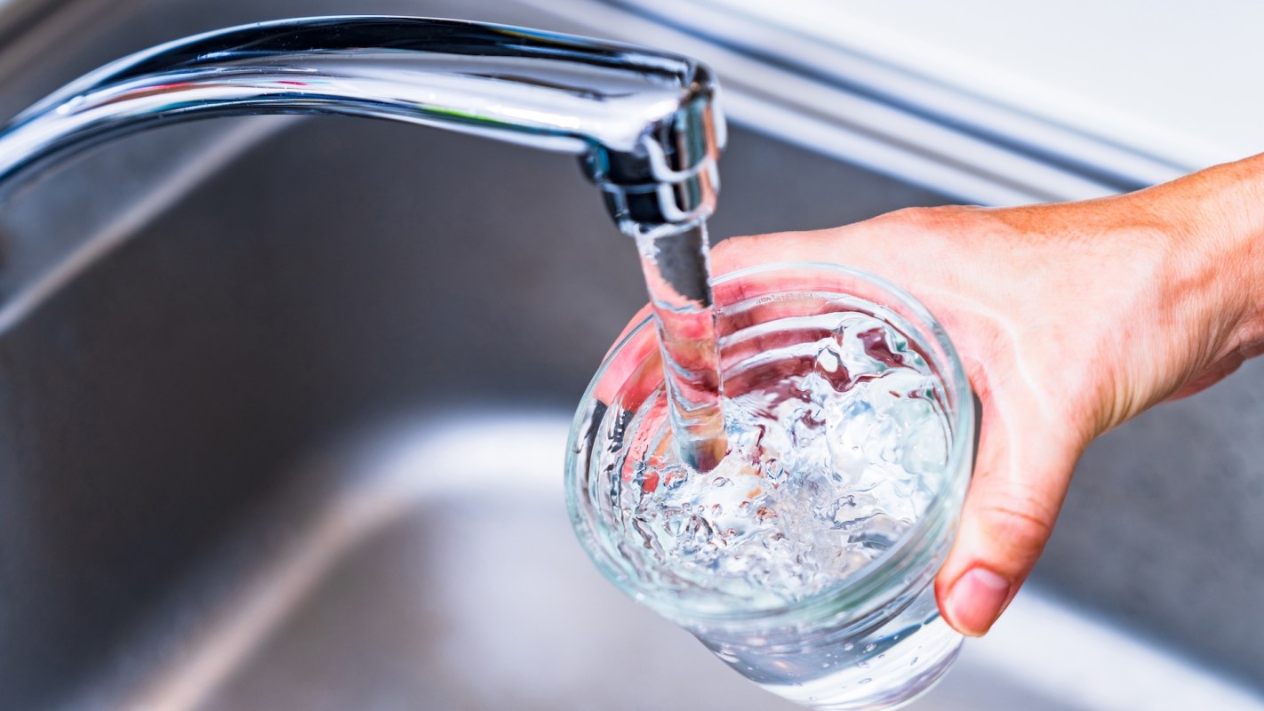 A hand filling a glass with water from a kitchen faucet.