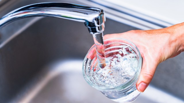 A hand filling a glass with water from a kitchen faucet.