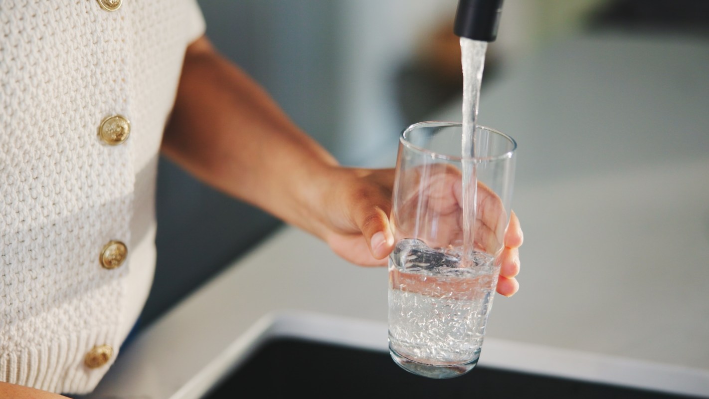 A person fills a glass with water from a kitchen faucet.