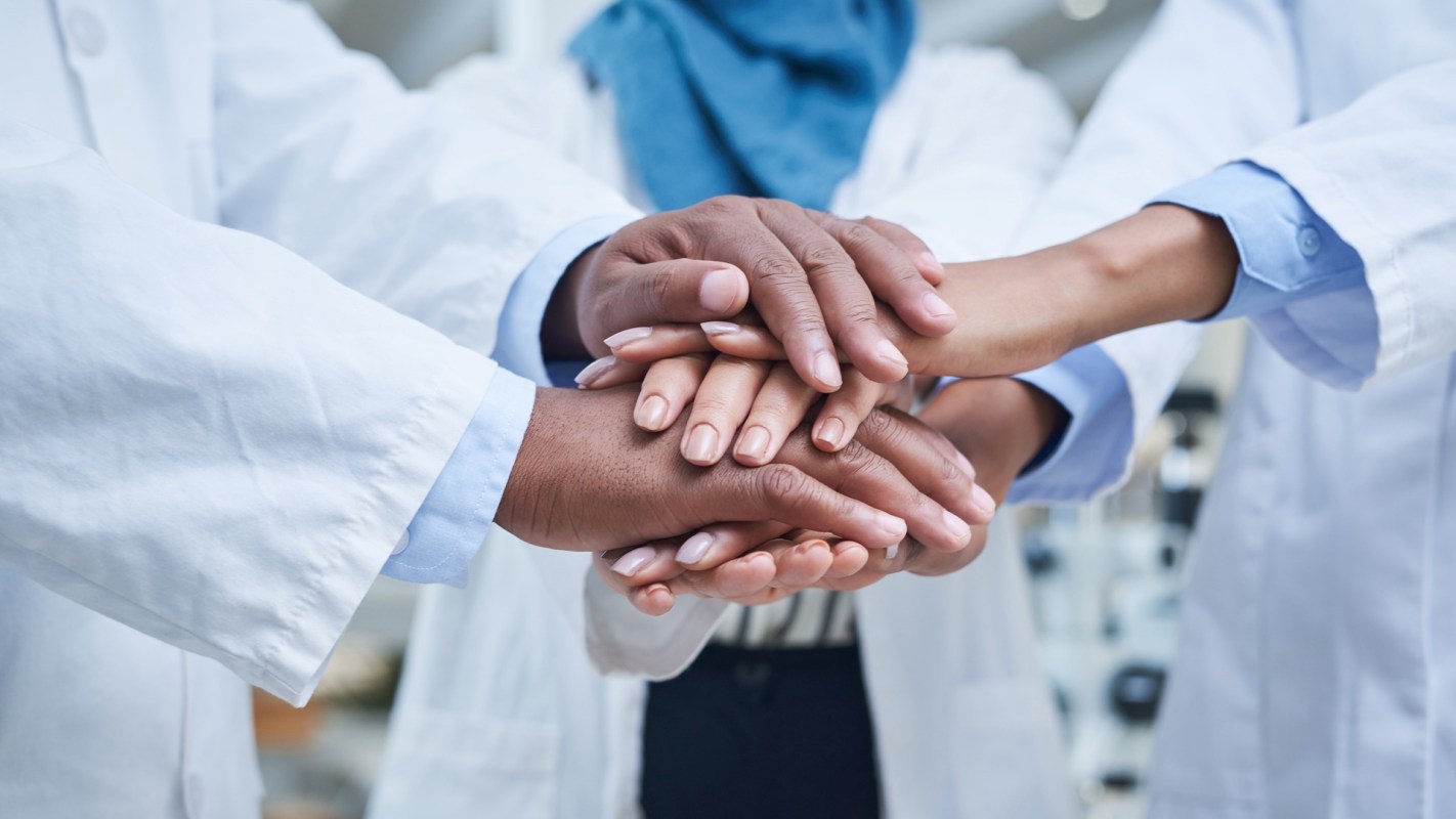 People in lab coats stacking their hands together.