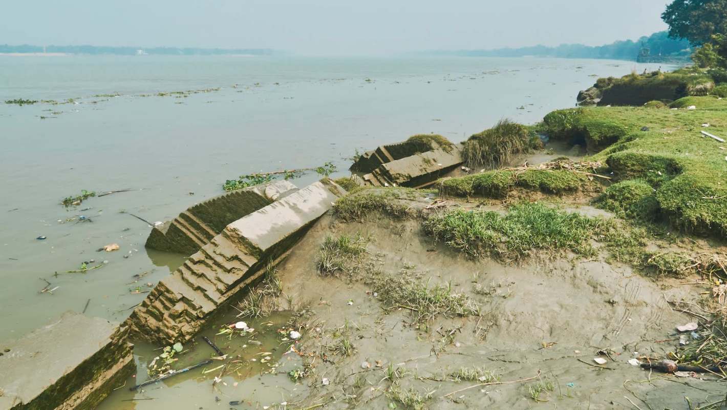 Riverbank with mud, grass, and scattered debris along the water's edge.