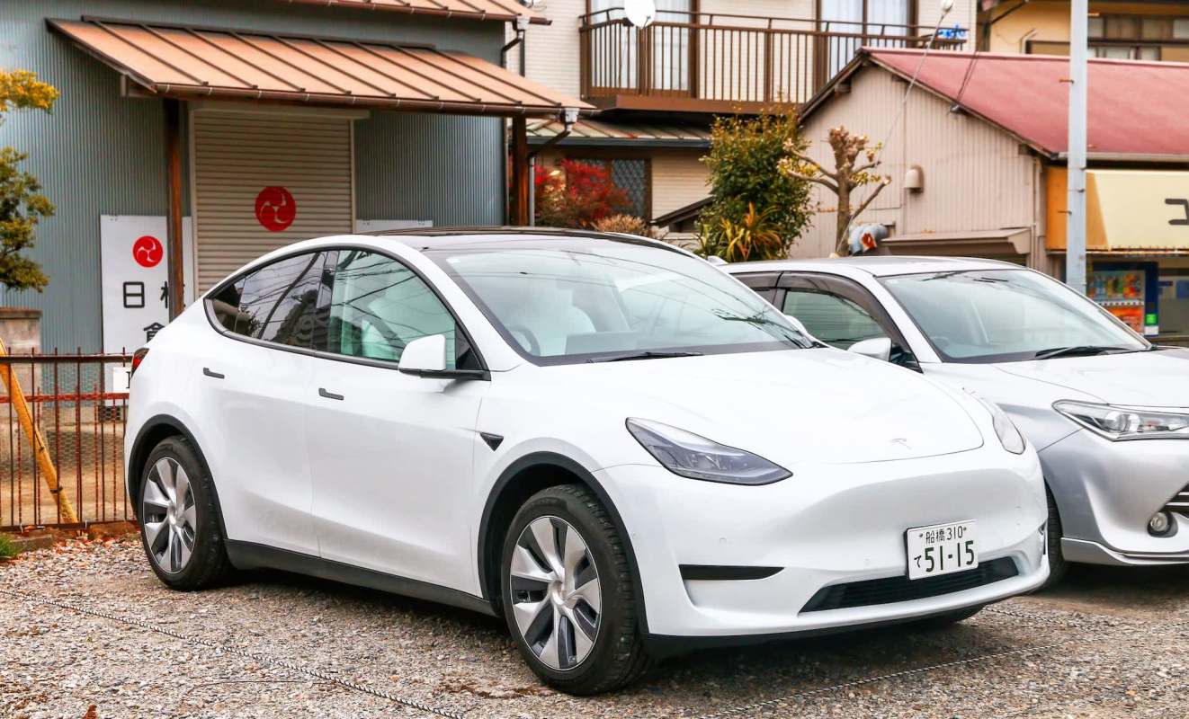 A white Tesla Model Y parked alongside another vehicle in an outdoor area.