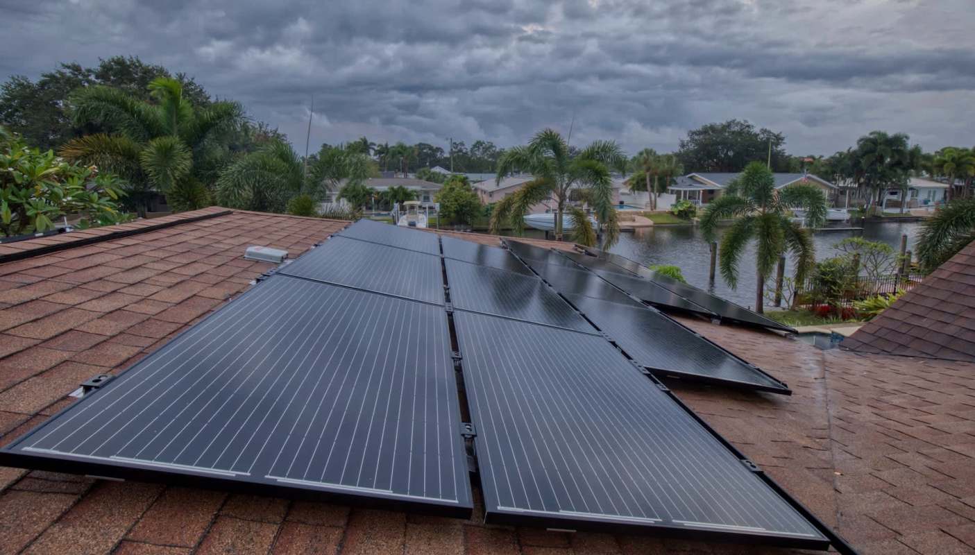 Solar panels installed on a rooftop overlooking palm trees and a waterway.