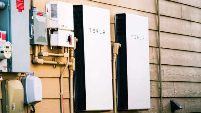 Two Tesla powerwall battery storage units mounted on a wall alongside electrical equipment.
