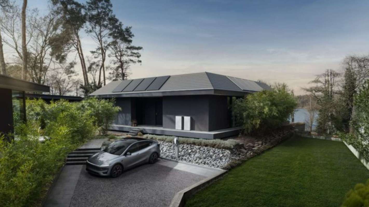 A modern house with solar panels surrounded by greenery and a parked electric car.