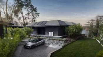 A modern house with solar panels surrounded by greenery and a parked electric car.