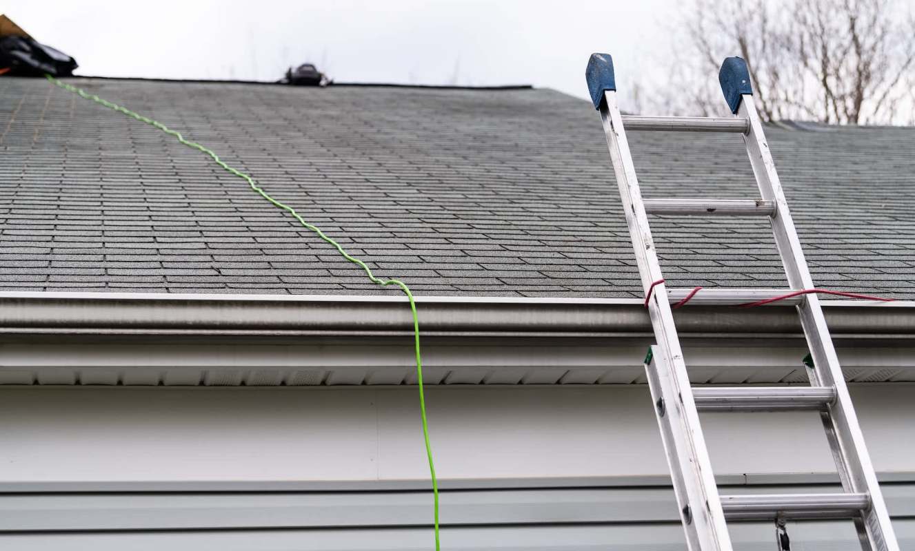 A ladder leaning against a house next to a roof with green cord and shingles.