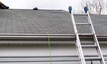 A ladder leaning against a house next to a roof with green cord and shingles.