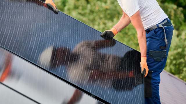 A person installs a solar panel on a roof.