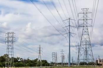 Multiple power towers and lines extend across a landscape under a cloudy sky.