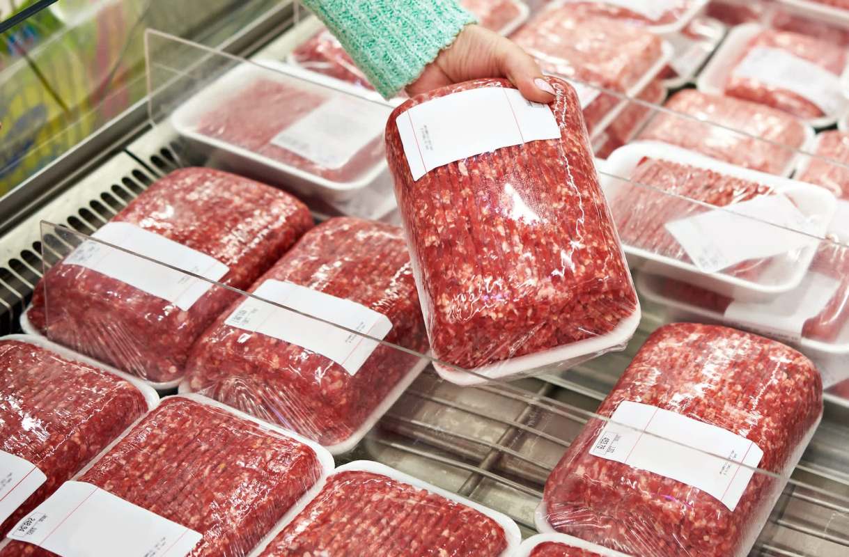 A hand retrieves packaged ground meat from a display case in a grocery store.