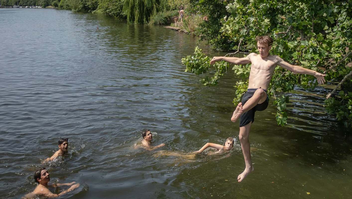 A boy jumps into a river while others swim nearby.